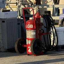 Load image into Gallery viewer, Red aviation wheeled fire extinguisher on a concrete airport surface, people in the background.